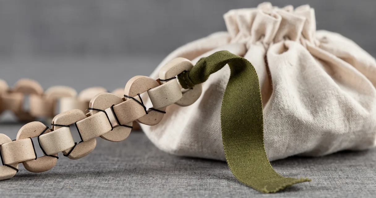A folded paper chain has a long olive cloth branch resting against a pleated linen form